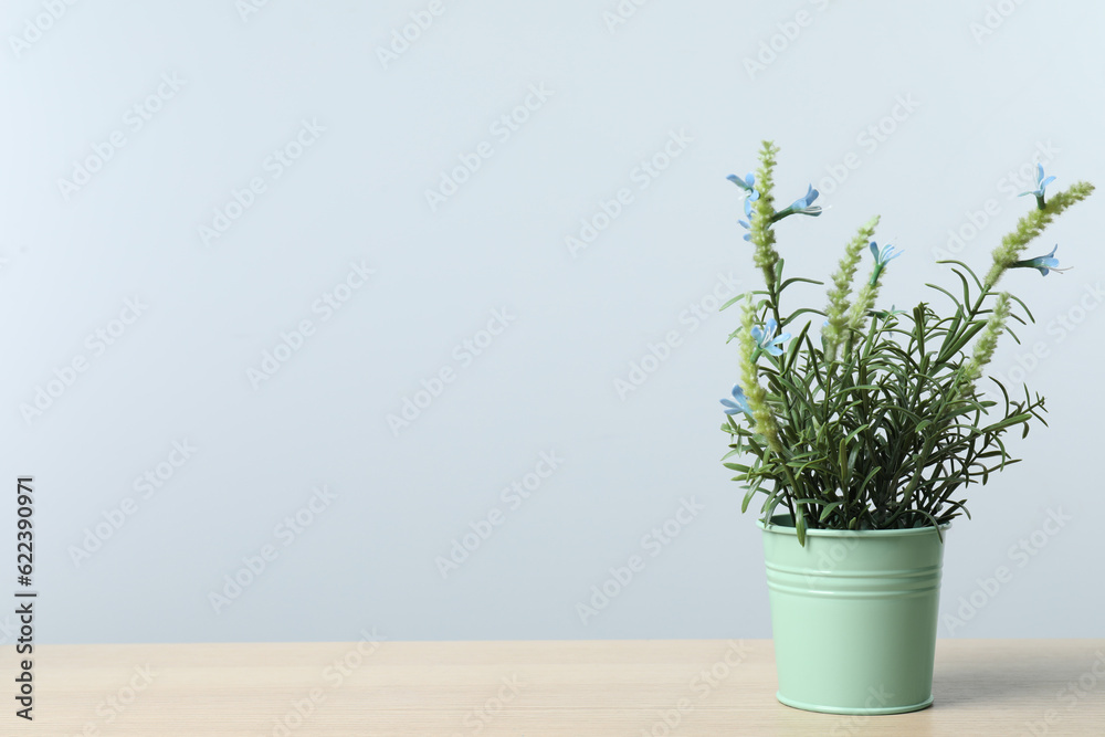 Beautiful artificial plant in flower pot on wooden table against light grey background, space for text