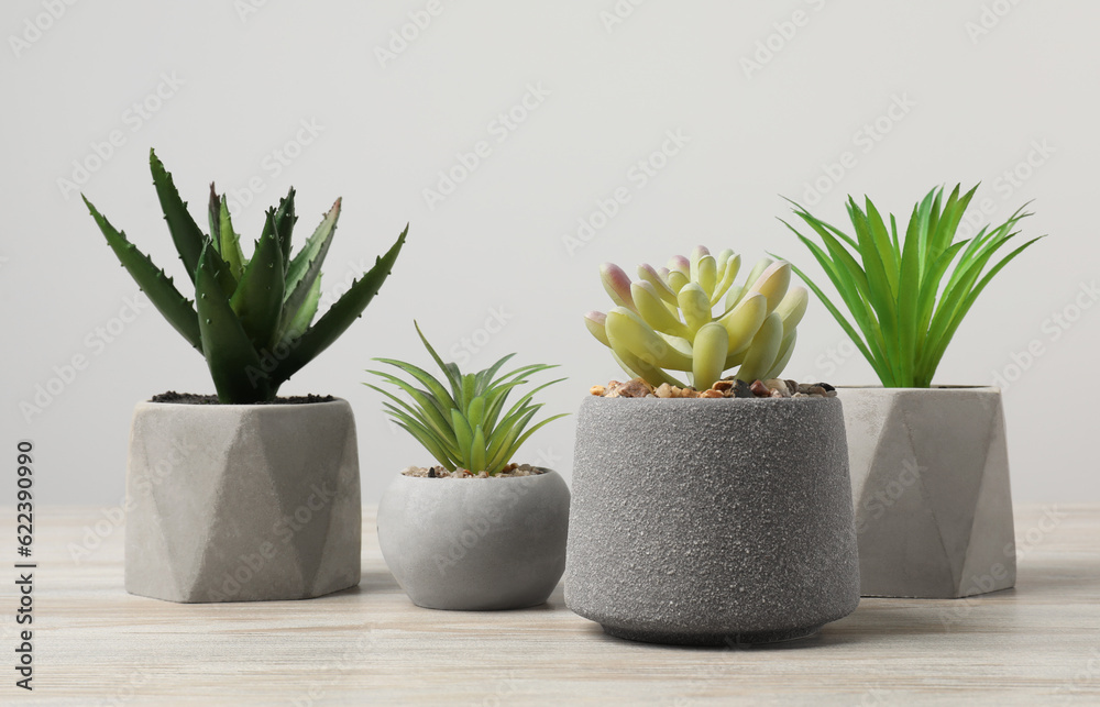 Many different artificial plants in flower pots on wooden table against light grey background Many different artificial plants in flower pots on wooden table against light grey background