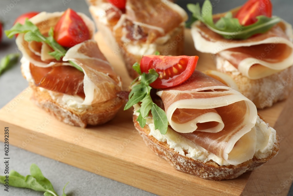 Tasty sandwiches with cured ham, tomatoes and arugula on wooden board, closeup Tasty sandwiches with cured ham, tomatoes and arugula on wooden board, closeup