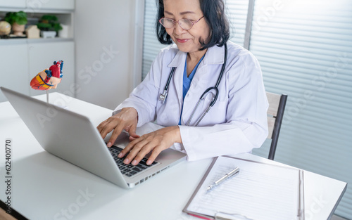 Cardiologist supports the heart senior asian woman doctor wearing glasses and uniform. portrait of mature old asian woman medic professional