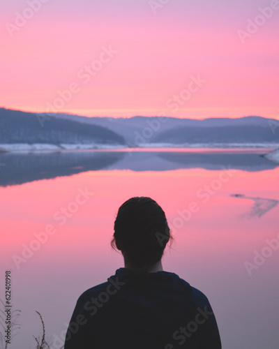 Woman looking at a pink sunrise on the horizon of Tygart Lake, West Virginia
