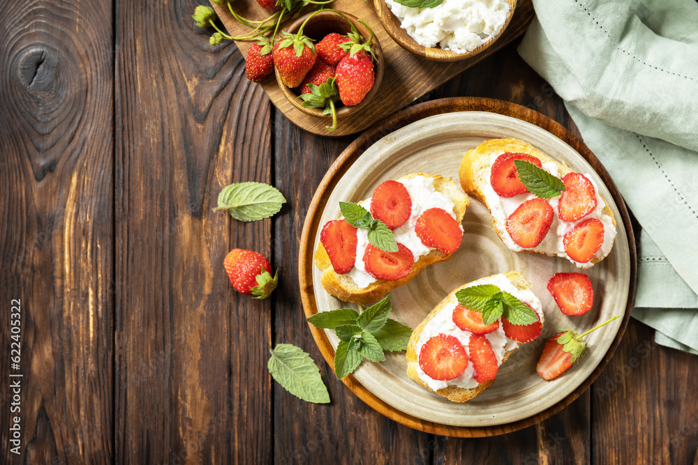 Sandwich with strawberries and soft cheese on wooden background. Berries toast breakfast, healthy food. View from above.