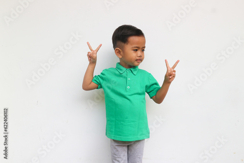 A smiling toddler boy raised hand to show two finger sign, isolated on white background