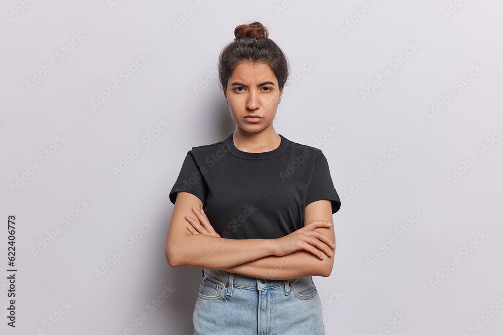 Serious offended woman adopts closed posture with folded arms exuding air of discontent frowns face wears casual black t shirt jeans isolated over white background. I dont want to speak with you Serious offended woman adopts closed posture with folded arms exuding air of discontent frowns face wears casual black t shirt jeans isolated over white background. I dont want to speak with you