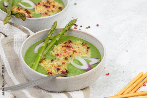 Vegetarian green soup puree with asparagus  and onion in bowl with a spoon closeup