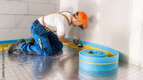 A roll of blue dilatation tape laid on the underfloor insulation. Soft focused Worker on the background during sticking tape to the wall. photo