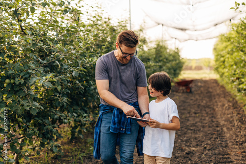 Father and son are working together in the orchard with tablet device. © cherryandbees