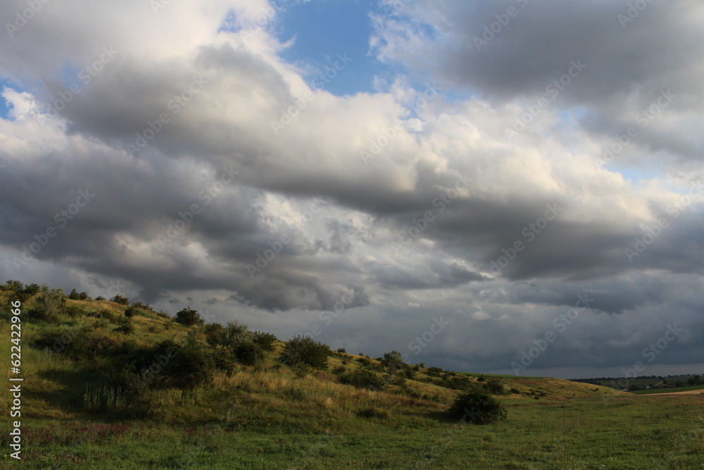 A green hill with bushes and clouds A green hill with bushes and clouds