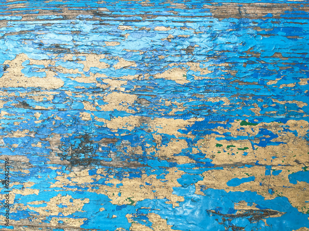 Old peeled wooden lath painted with blue paint, close-up, top view. The surface of the lath is cracked, worn, with large and small cracks.