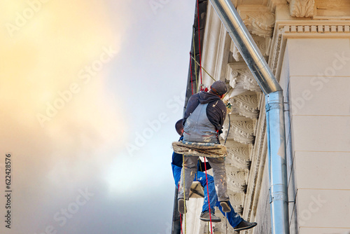 Canvastavla Worker on hanging on rope and paint facade wall of historic building