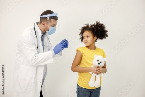 Male doctor doing a vaccination to a black girl isolated on white backgriound photo