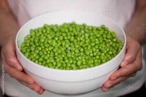 Woman holding a large bowl of sweet green peas. Selective focus.