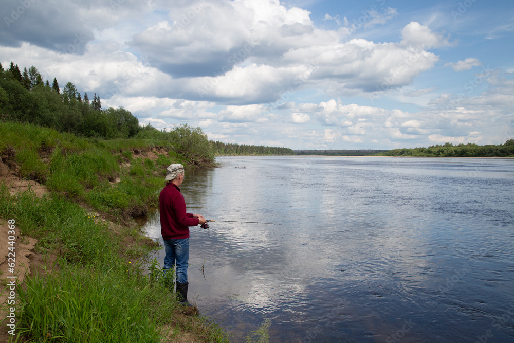 A man is fishing on the river in the summer.Landscape and with clouds on the river.