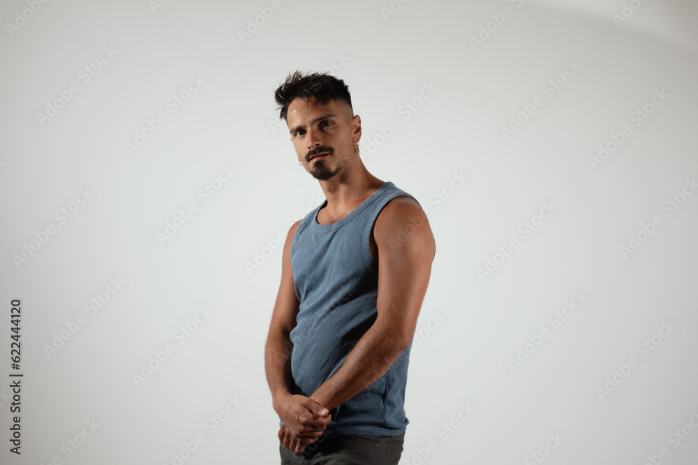 Standing in a studio, a man stands with his hands clasped in front. He ...