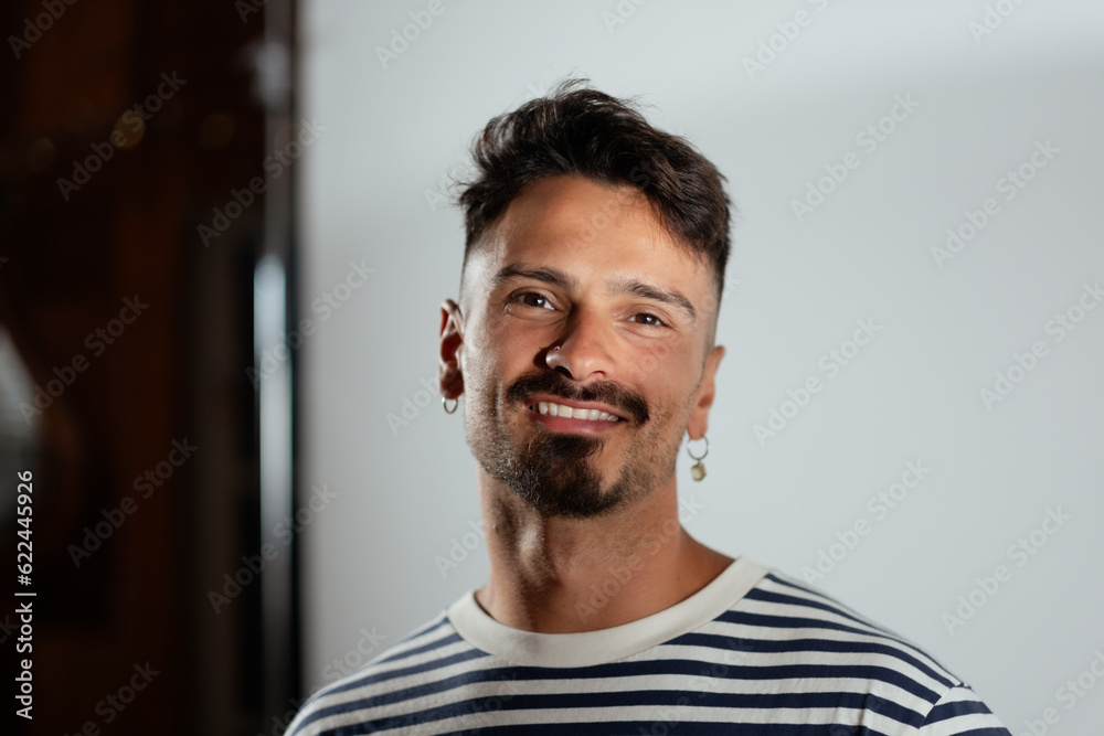 Fototapeta premium With a goatee and an earring, an adult man poses for a portrait in a studio space.
