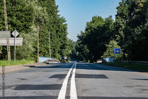 Asfaltowa droga idąca przez most nad rzeką Odrą otoczona barierkami wokół oświetlenie uliczne oraz nieliczne drzewa a na tle błękitne lekko zachmurzone niebo w zachodniej Polsce	