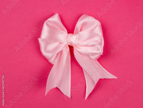 Light pink satin ribbon bow isolated on pink background, close up.
