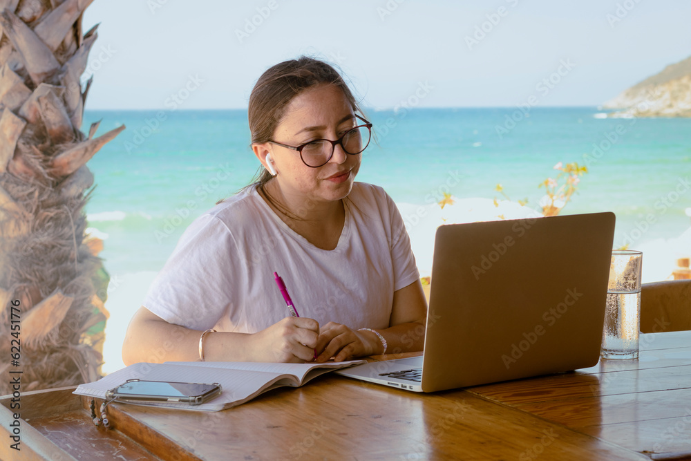 young girl working and meeting at the beach wearing glasses and phones with a laptop
