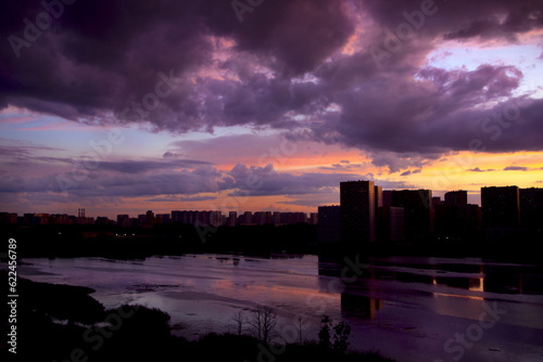 city houses on the lake at sunset, thunderclouds