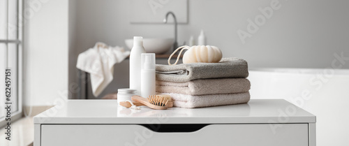 Fotografering Stack of towels, cosmetics, loofah and brushes on chest of drawers in bathroom