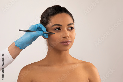 Plastic surgeon hands making preparation lines on black woman face