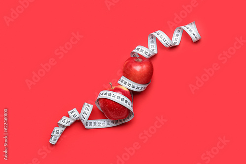 Apples and measuring tape on red background. Diet concept