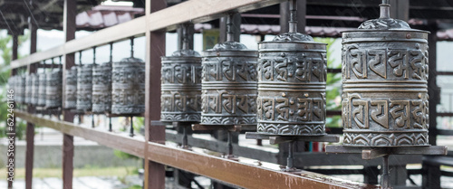 A row of prayer drums decorated with Buddhist symbols and writings on the territory of the datsan, a Buddhist temple. Religious prayer wheel for meditation in a Buddhist temple in Buryatia.Banner