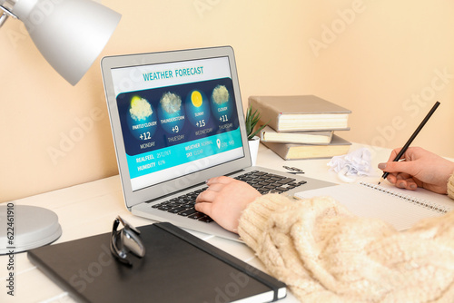 Woman with laptop checking weather forecast at table, closeup