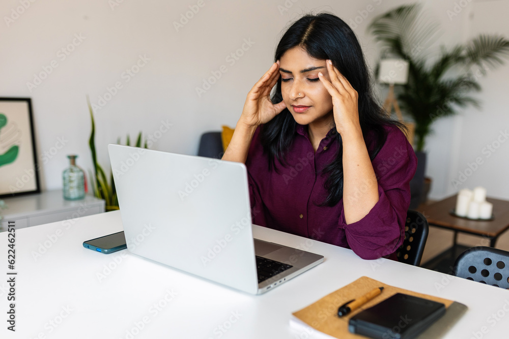 Young indian woman suffering from a headache or migraine while working on laptop computer at home. Young indian woman suffering from a headache or migraine while working on laptop computer at home.