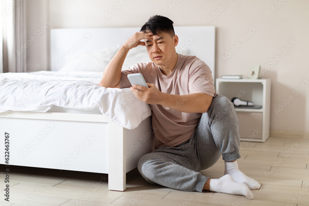 Unhappy depressed chinese businessman using phone in bedroom