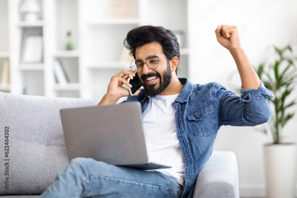 Overjoyed Indian Guy With Laptop And Cellphone Celebrating Success At Home