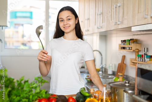 Young attractive housewife cooking soup in kitchen, holding spoon in her hand photo