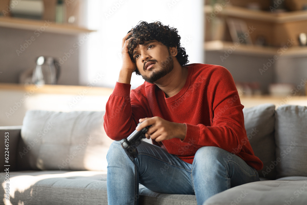 Upset Indian Man With Joystick In Hand Sitting On Couch At Home Upset Indian Man With Joystick In Hand Sitting On Couch At Home