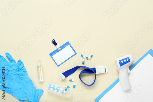 Badge, tourniquet, pills, infrared thermometer, medical gloves and clipboard on beige background photo