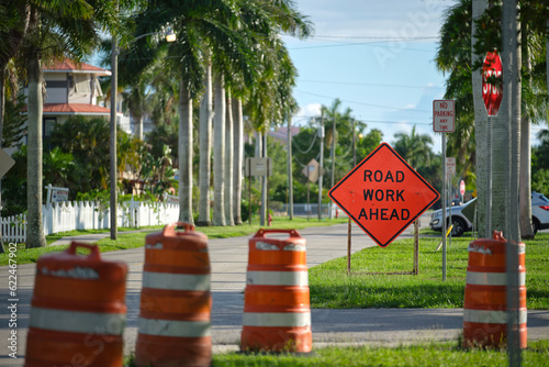 Road work ahead sign and barrier cones on street site as warning to cars about construction and utility works