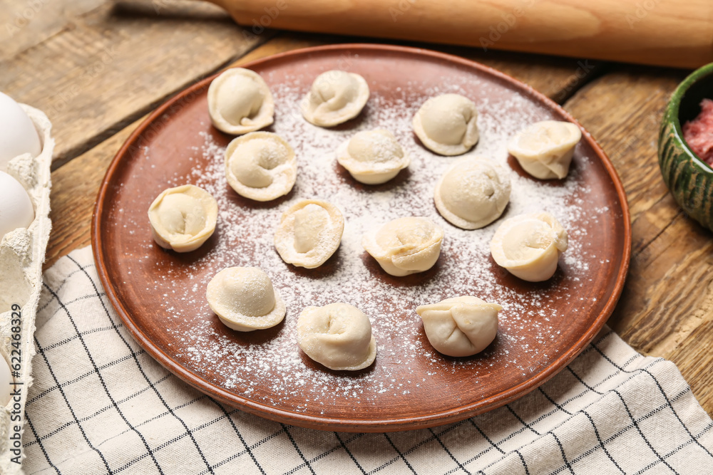 Plate with uncooked dumplings on wooden background Plate with uncooked dumplings on wooden background