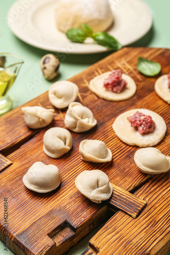 Wooden board with uncooked dumplings on table