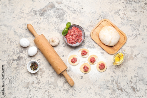 Raw dough with minced meat and ingredients for preparing dumplings on beige background