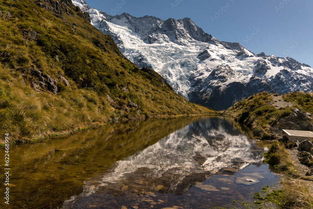 The small alpine tarn at the summit of the Sealy Tarns track with mirror reflections of the snow covered mountains in the Aoraki Mt Cook National park