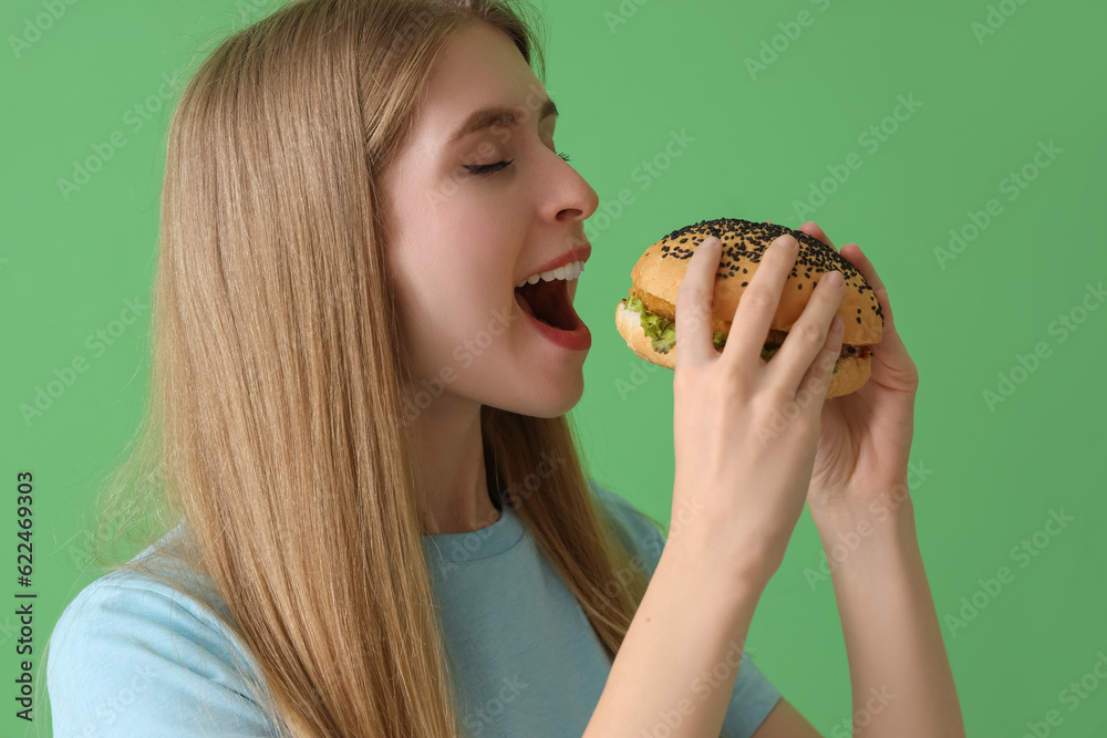 Young woman with tasty burger on green background, closeup