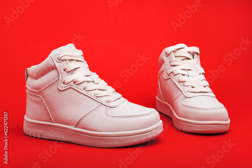 pair of white youth sneakers on red background close-up.