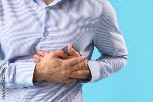 Young man having heart attack on blue background, closeup
