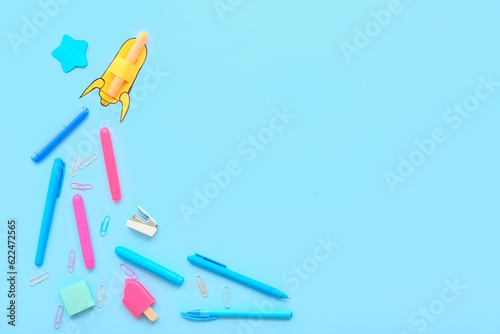 Creative composition with paper rocket and different stationery on blue background
