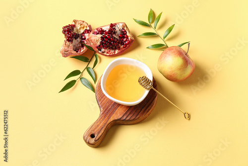 Wooden board with bowl of honey, pomegranate and apple for Rosh Hashanah celebration (Jewish New Year) on yellow background photo