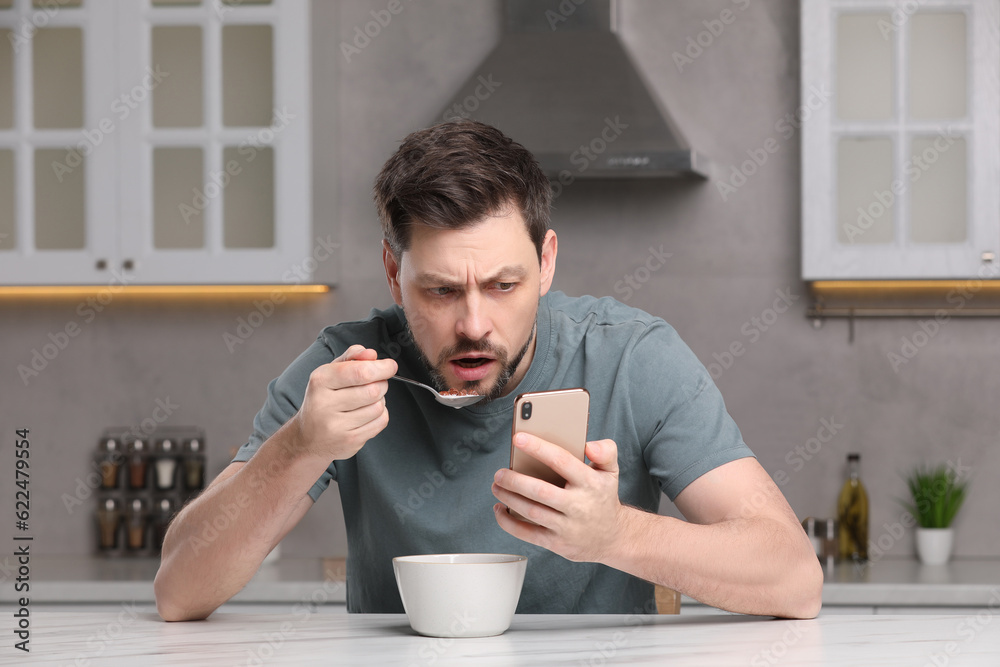 Man using smartphone while having breakfast at table in kitchen. Internet addiction Man using smartphone while having breakfast at table in kitchen. Internet addiction