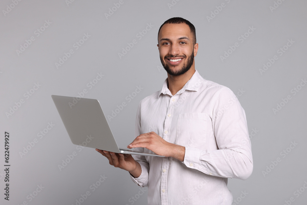 Smiling young man with laptop on grey background Smiling young man with laptop on grey background