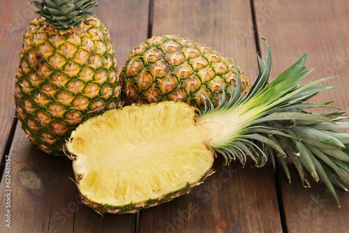 Whole and cut ripe pineapples on wooden table, closeup