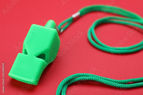 One green whistle with cord on red background, closeup