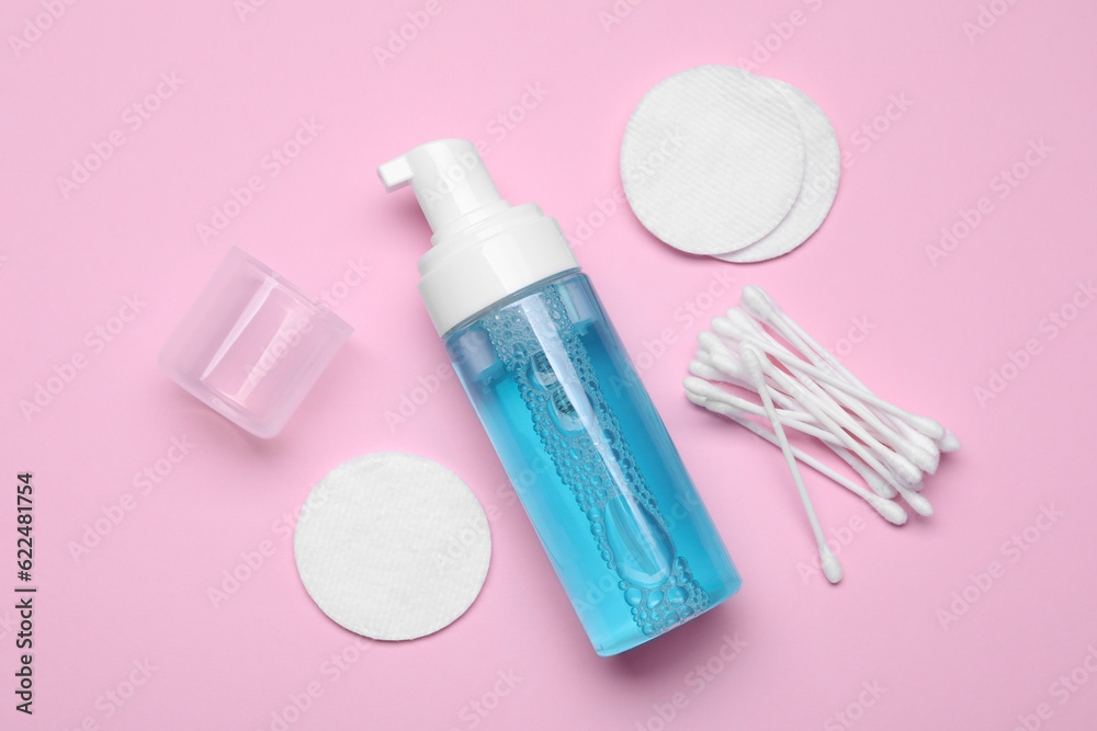 Bottle of face cleansing product, cotton buds and pads on pink background, flat lay. Space for text Bottle of face cleansing product, cotton buds and pads on pink background, flat lay. Space for text