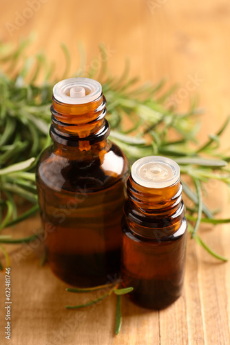 Bottles of rosemary oil and fresh twigs on wooden table, closeup